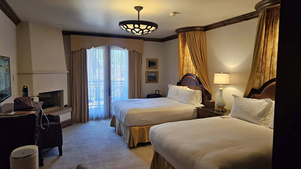 Guest room with two beds, a fireplace, a patterned armchair and balcony doors with sheer curtains