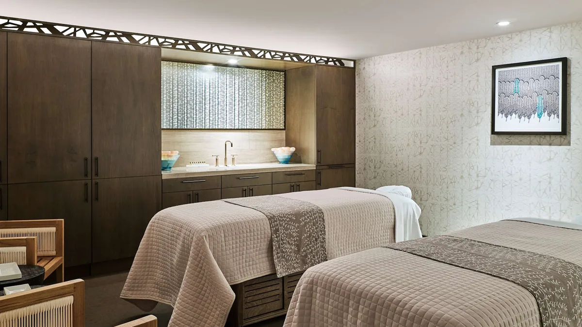 Spa treatment room with two massage tables, a wall of dark cabinets and a framed abstract picture