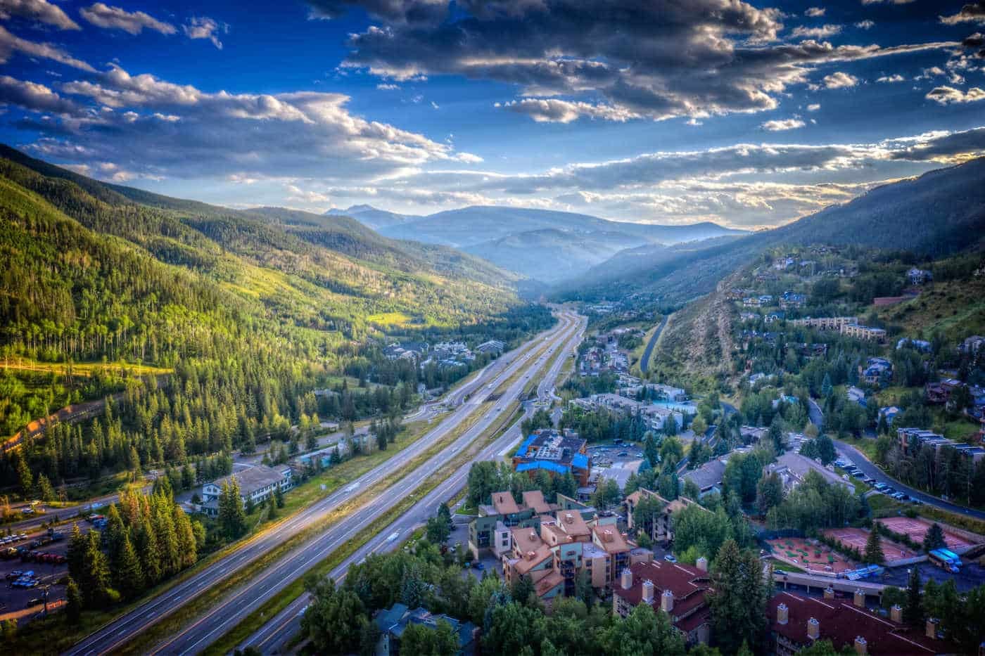 Aerial view of the Vail valley in summer, with Interstate 70 running between forested mountainsides and lodging buildings beside the highway