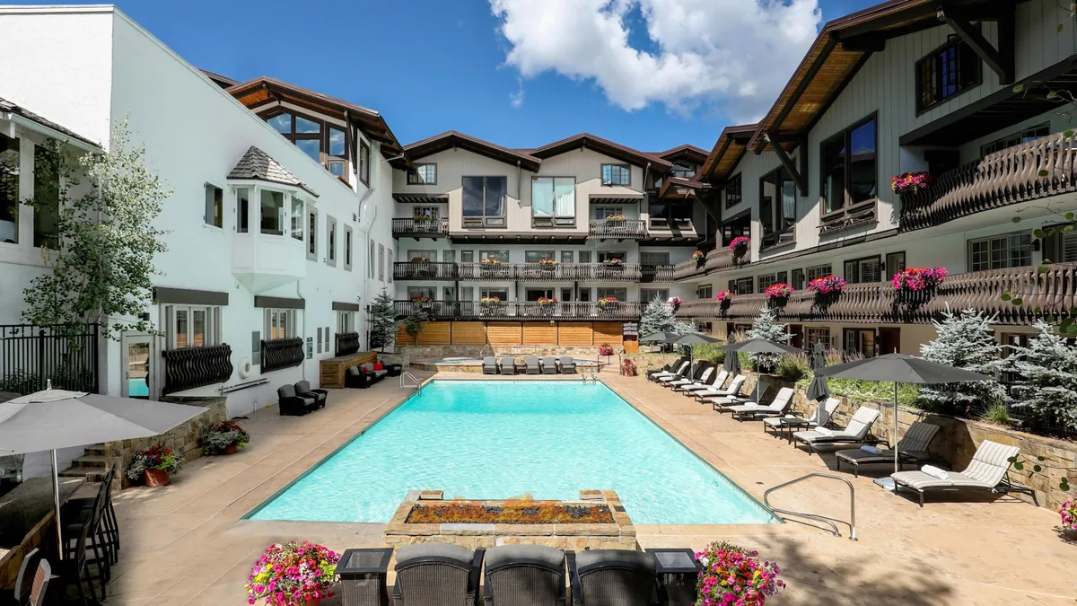 Outdoor pool courtyard with lounge chairs and umbrellas, surrounded by white and timber-framed hotel buildings with flower boxes