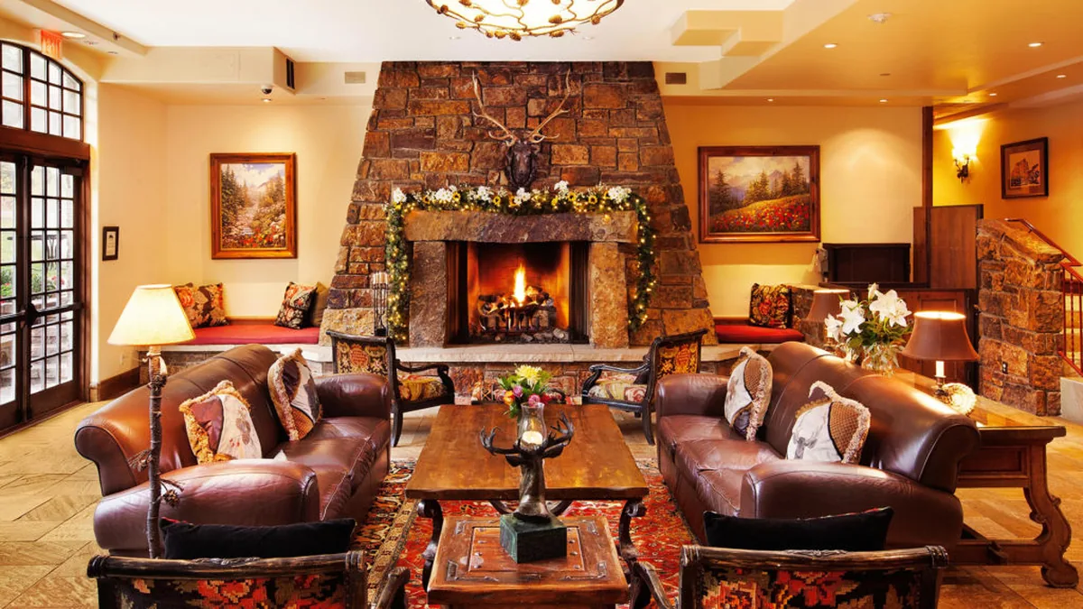 Lobby sitting area with two leather sofas facing a stone fireplace with a lit fire and an antler mount above it