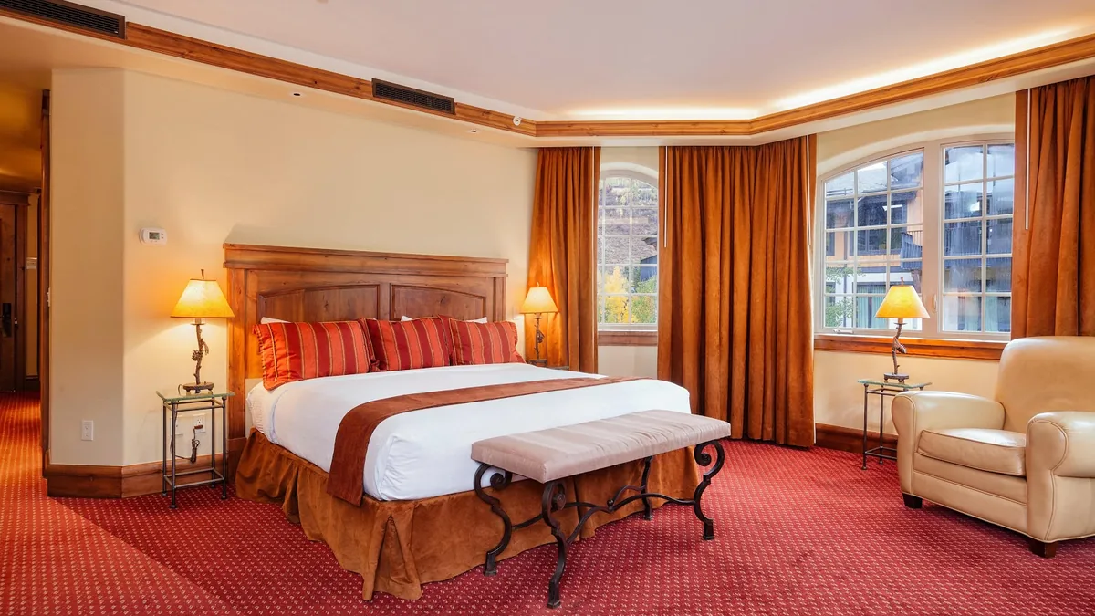 Guest room with a king bed, a wooden headboard, red-striped bedding, gold drapes and an armchair by arched windows