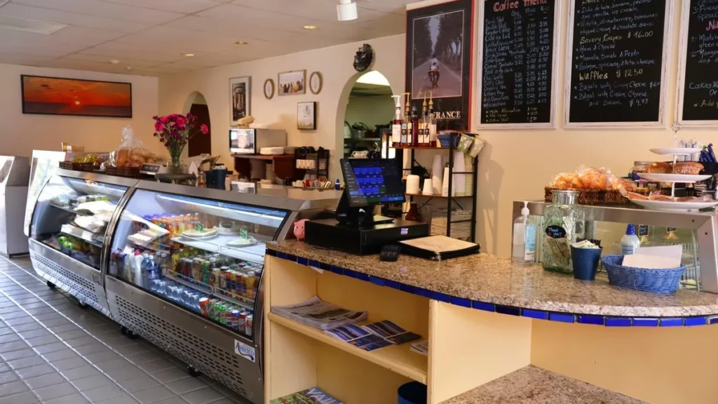 Deli counter with a glass display case, pastries and chalkboard menus at Les Délices de France